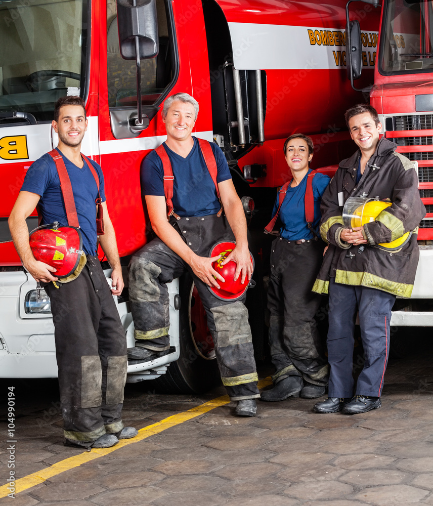 Fototapeta premium Portrait Of Smiling Firefighters Leaning On Trucks
