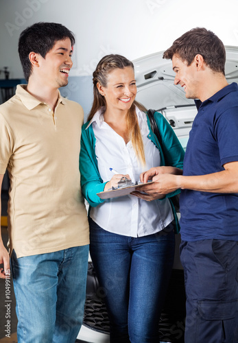 Mechanic Taking Sign On Document From Happy Couple