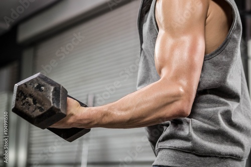 Muscular man with grey jumper lifting dumbbell