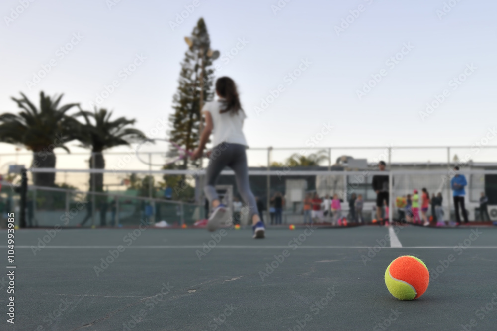 Tennis ball on background of young girl playing tennis on a court