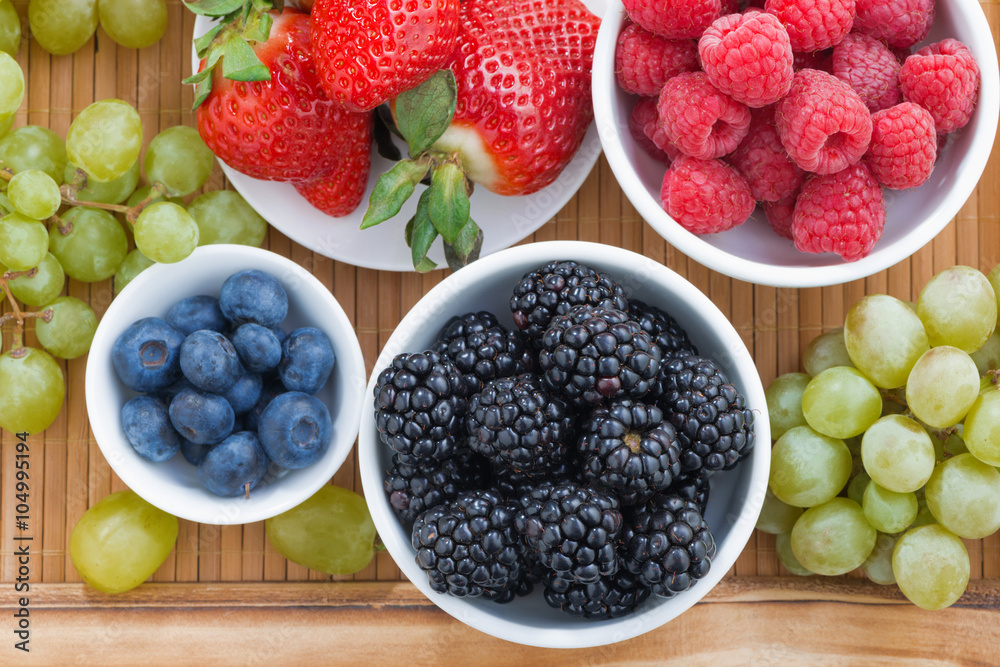 fresh berries in a bowl and green grapes on wooden tray fresh berries in a bowl and green grapes on wooden tray