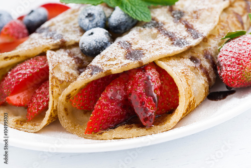 crepes with fresh berries and chocolate sauce on plate, closeup