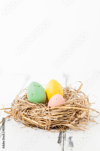 tre pastellfärgade ägg i ett fågelbo på vit trä bakgrund