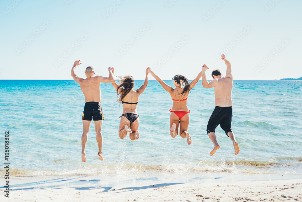 Rear view of a multiethnic group of friends jumping into water d