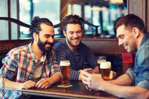 male friends with smartphone drinking beer at bar