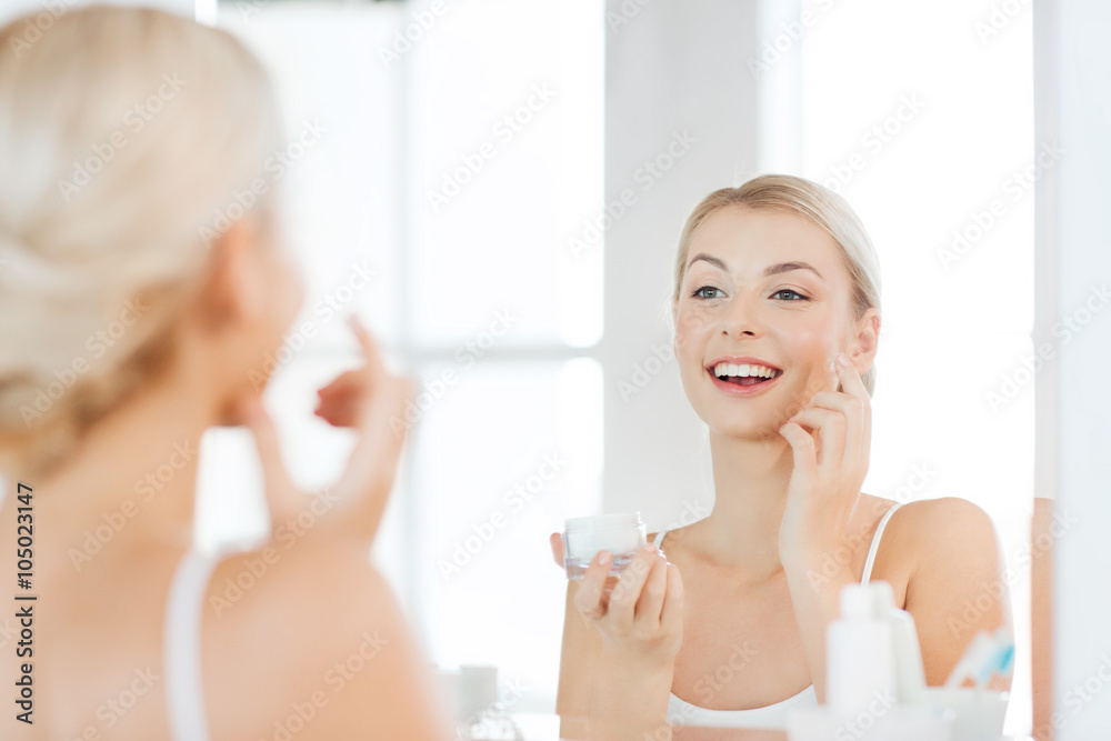 happy woman applying cream to face at bathroom happy woman applying cream to face at bathroom