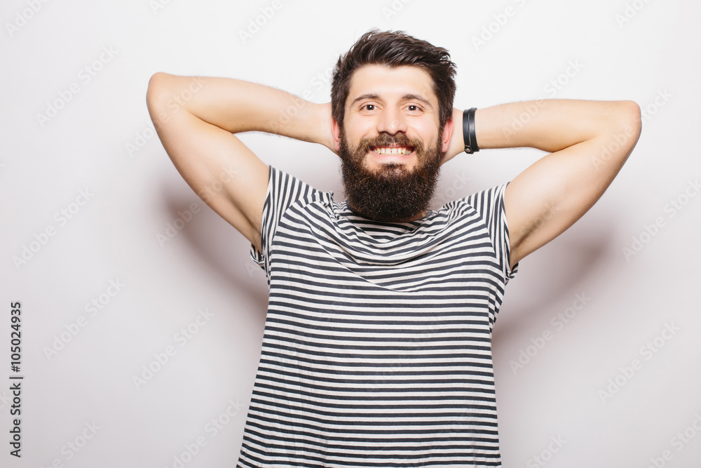 Handsome young man with beard holding hands behind head and smiling while standing against white background Handsome young man with beard holding hands behind head and smiling while standing against white background