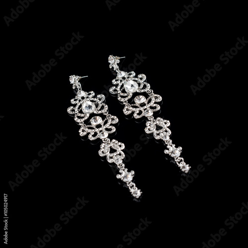 Long silver or white gold earrings with diamonds and crystals on black reflective background.