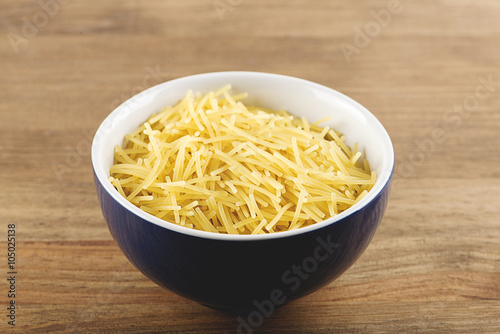 Blue bowl with uncooked noodles on wooden table