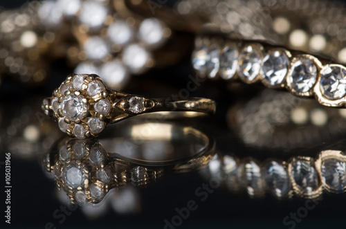 Gold jewelry with diamonds on blackboard. Gold diamond jewelry on a black background. Jewelry is reflected on the mirror surface. Rings and bracelets.