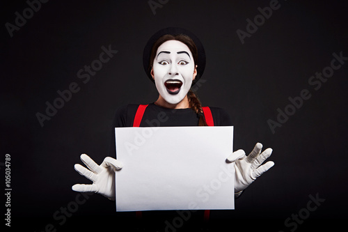 Smiling female mime holding white sheet of paper/ Crazy smiling girl mime holding white sheet of paper on black background