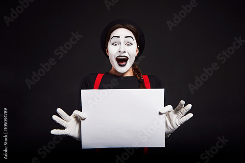 Smiling female mime holding white sheet of paper/ Crazy smiling girl mime holding white sheet of paper on black background photo