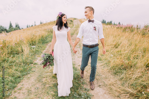 Beautiful wedding couple hold hands and walks on path n mountains