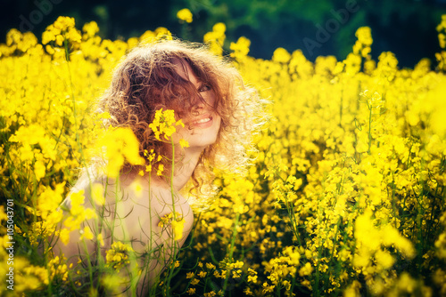 Happy red-haired beautiful girl laughing in yellow flowers on the field