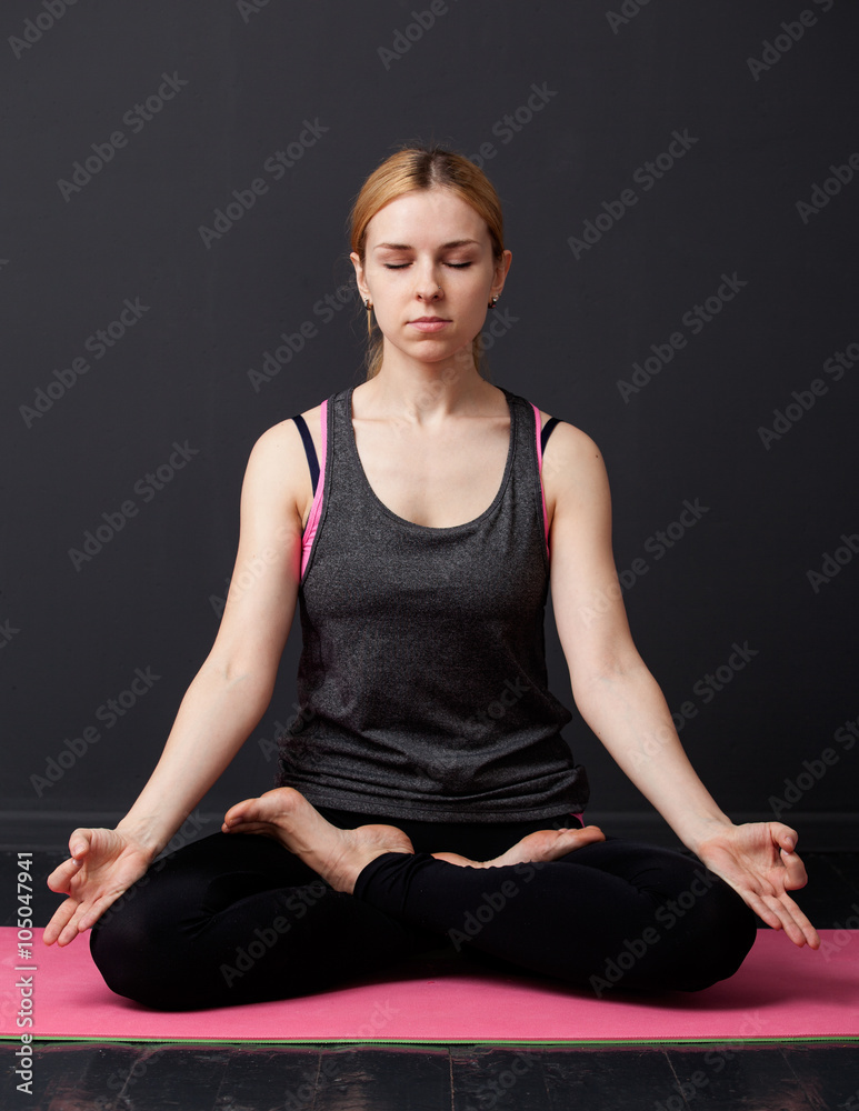 Fototapeta premium Young woman is sitting in the lotus pose with closed eyes