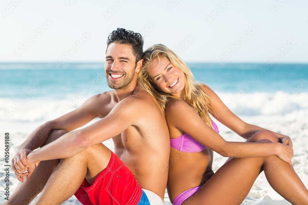 Happy couple sitting back to back on beach Happy couple sitting back to back on beach