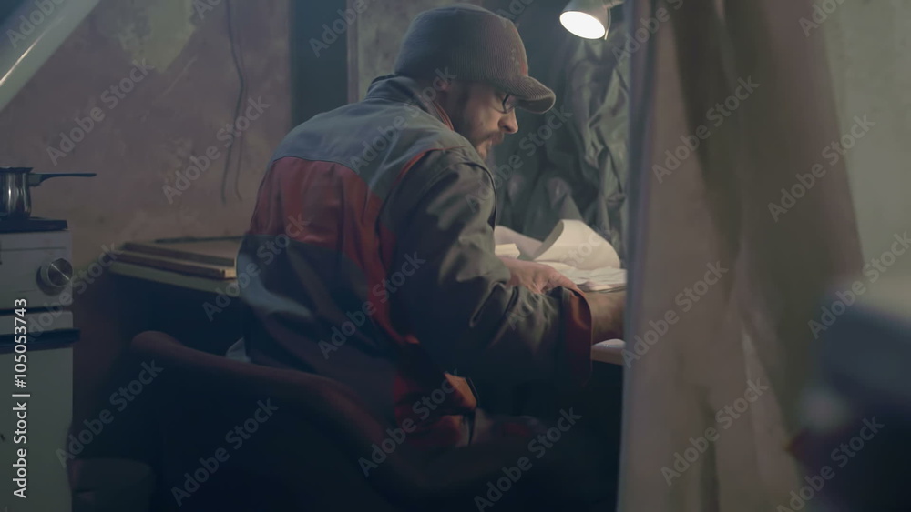 Man seating at the drawing table in the working shop drawing a blueprint and drinking coffee, footage in slow motion.
