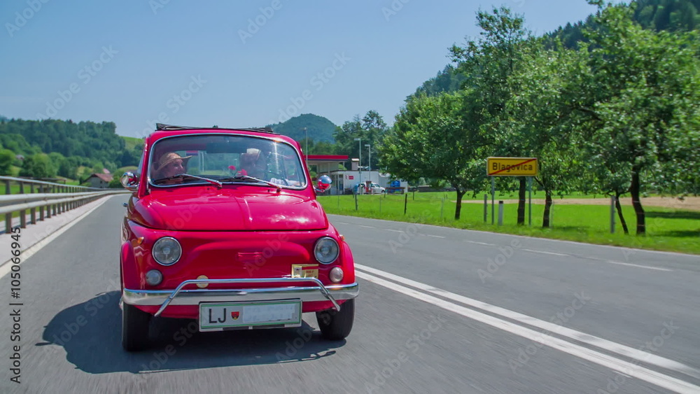 An old couple talking in a red vintage car