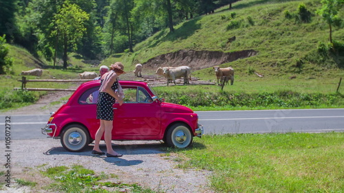 An older couple is going into their small vintage red car photo