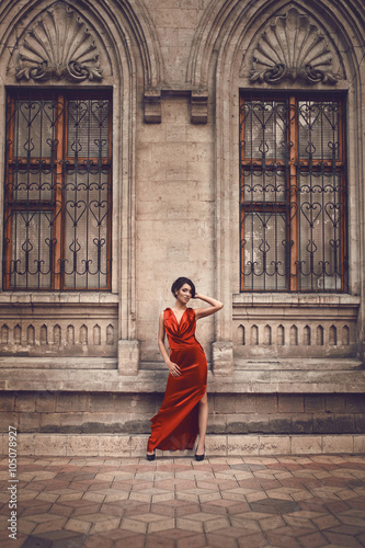 Gorgeous woman in red dress outside of old house