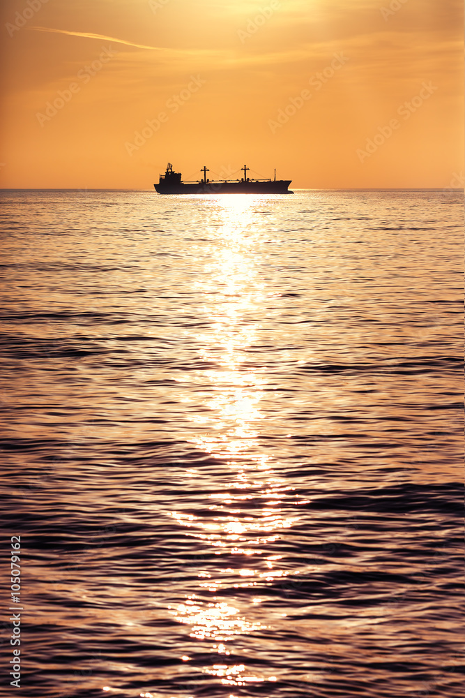 Cargo ship sailing on sunrise near the beach