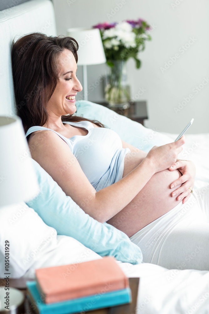 Pregnant woman lying in bed texting Pregnant woman lying in bed texting
