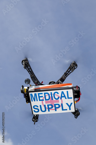 UAV drone quadrocopter with modern GPS navigation transporting box with medical supplies, against blue sky, space for text