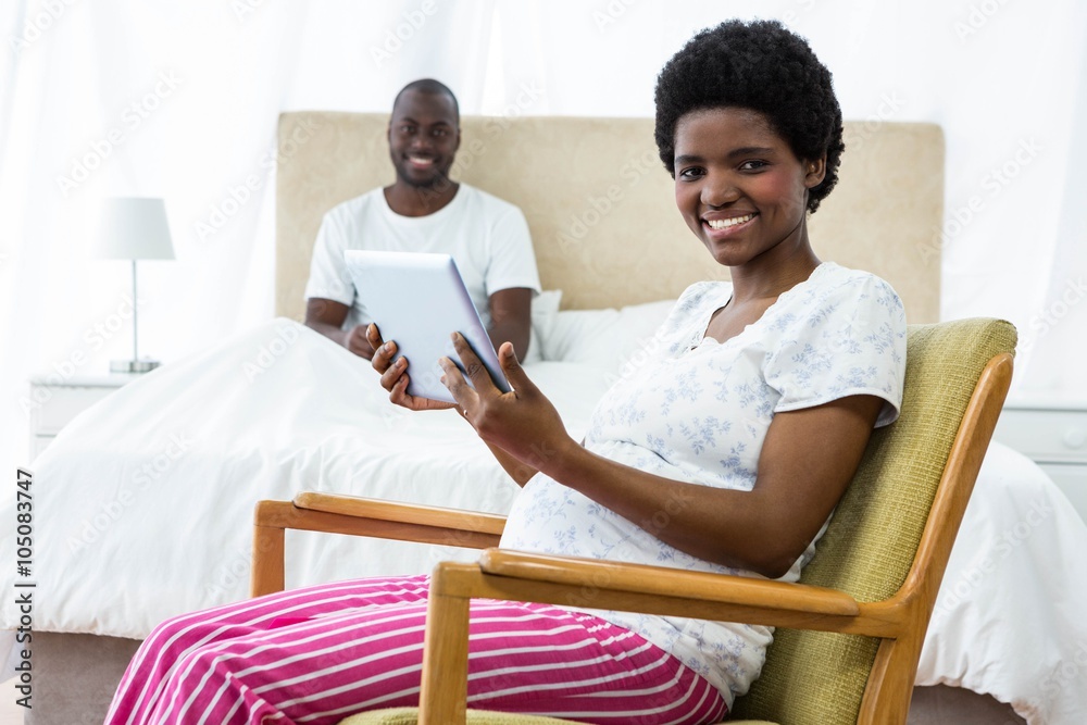 Pregnant woman using tablet on chair and man sitting Pregnant woman using tablet on chair and man sitting