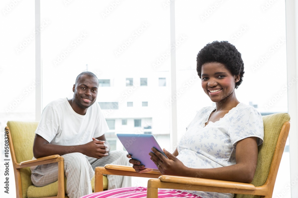 Smiling pregnant woman using tablet and man sitting Smiling pregnant woman using tablet and man sitting