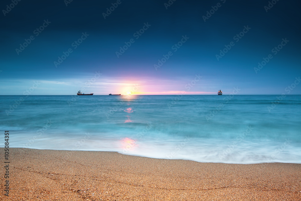 Cargo ship sailing on sunrise near the beach
