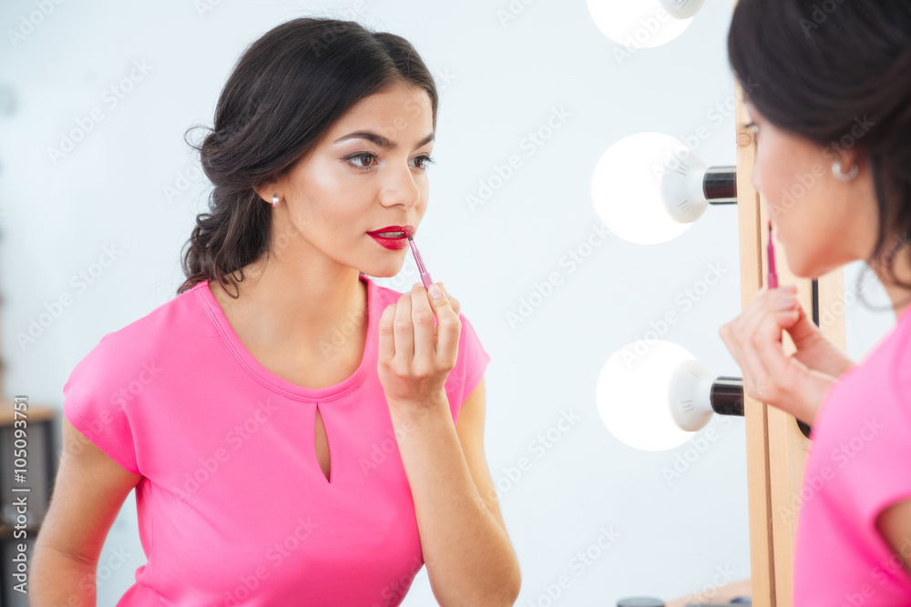 Attractive woman looking at mirror and applying red lipstick tolips Attractive woman looking at mirror and applying red lipstick tolips