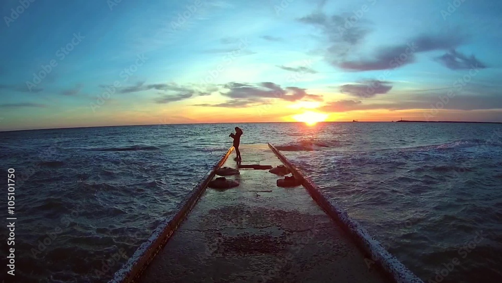 Video 1920x1080 - A wide-angle view of the concrete pier on a stormy day with a young woman standing on it and looking at the sunset over the Black Sea in winter Video 1920x1080 - A wide-angle view of the concrete pier on a stormy day with a young woman standing on it and looking at the sunset over the Black Sea in winter