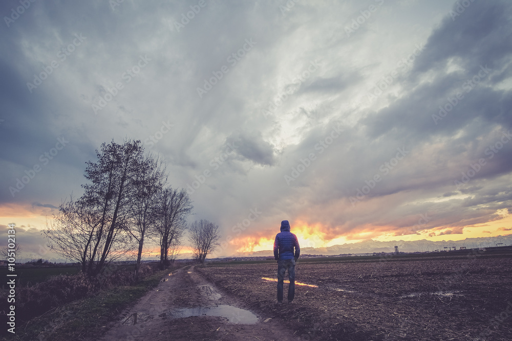 Fototapeta premium Man under a cloudy sky in the country watching the sunset