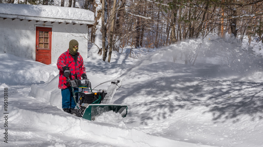 A Canadian man operating a snow throwing machine on a winter day after a snowstorm dumped 8 inches of snow.  Man operating a snow blower in Canada.