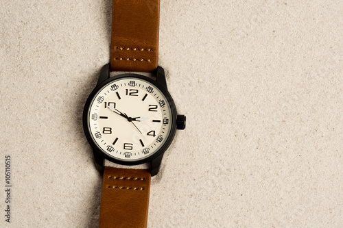 Watch with leather strap on sand background