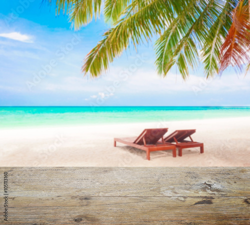 wood table top on blur beach background with beach chairs under coconut tree
