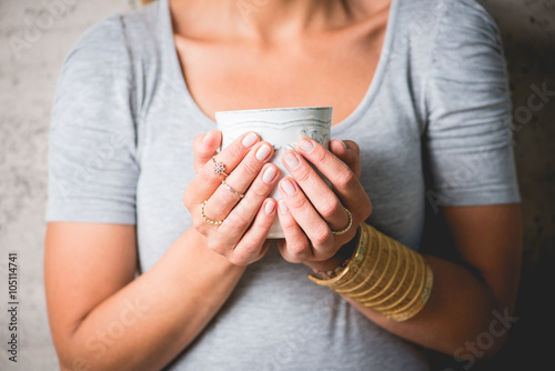 Woman holding a cup of tea or coffee. She is wearing stylish jewels on her fingers.