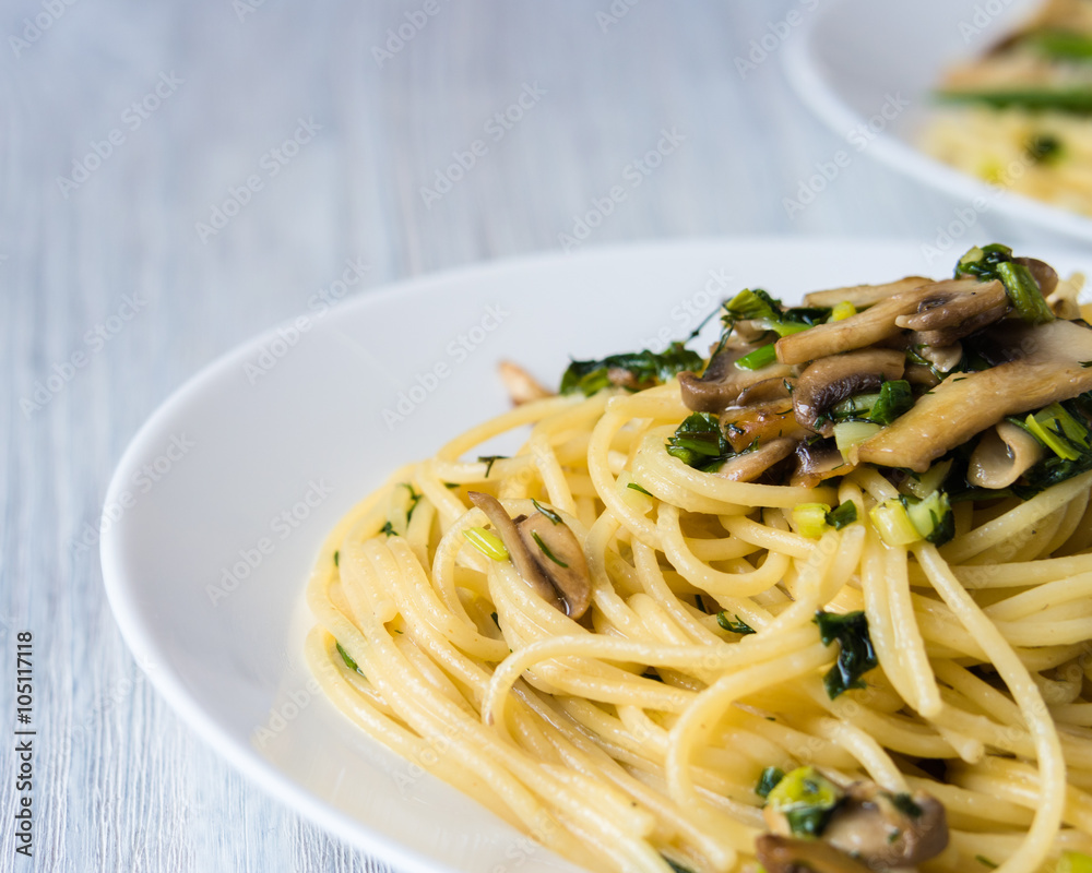 Two plates of pasta with mushrooms and green onions on a white p