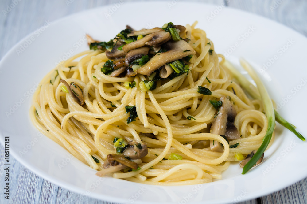 Pasta with mushrooms and green onions on a white plate on a wood
