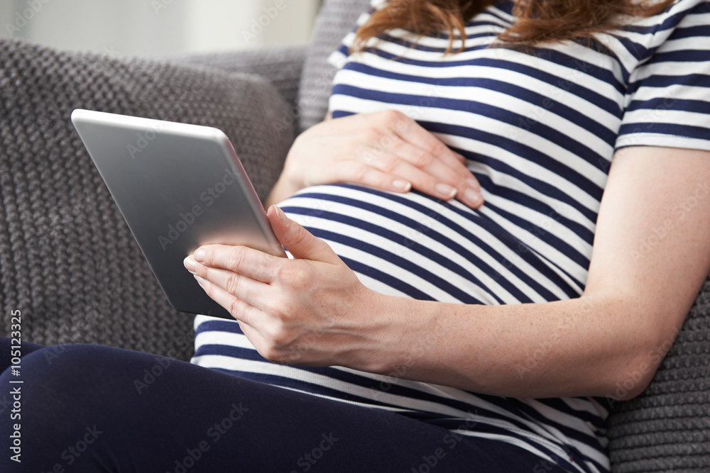 Close Up Of Pregnant Woman Using Digital Tablet At Home