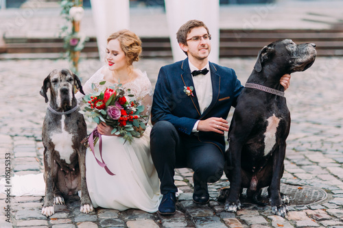 Photography Attractive wedding couple sitting on their haunches on the pavement and holding