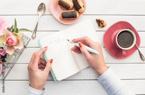 Woman hands drawing or writing with ink pen in open notebook on white wooden table. Bird eye view.