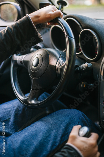 Close up of a man's hand on a steering wheel driving a car.