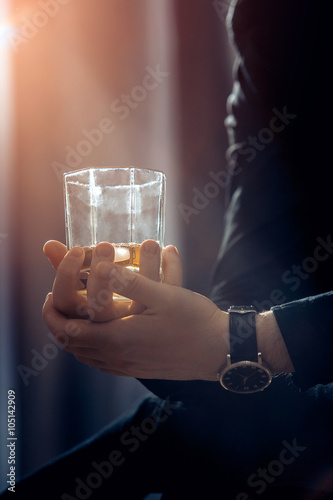Vertical photo of whiskey glass in the hands of business man that shined by warm light