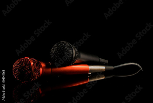 Two microphones lying on black surface. Black background, close up photo