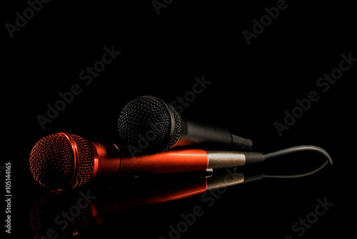 Two microphones lying on black surface. Black background, close up