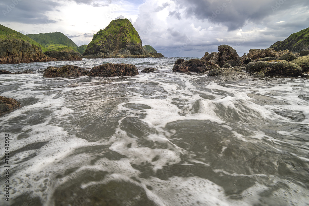 Natural rock with strong water wave and cloudy sunset background at Pantai Semeti Lombok, Indonesia.