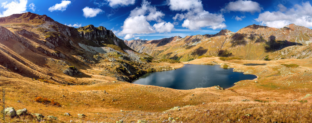 Alpine lake with the dark water fall of yellow among the rocky hills and cliffs in the Caucasus mountains