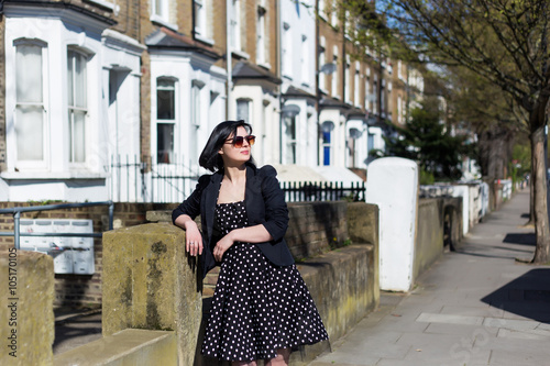 Girl in black dress with polka dots and sunglasses standing on the streets of London.
