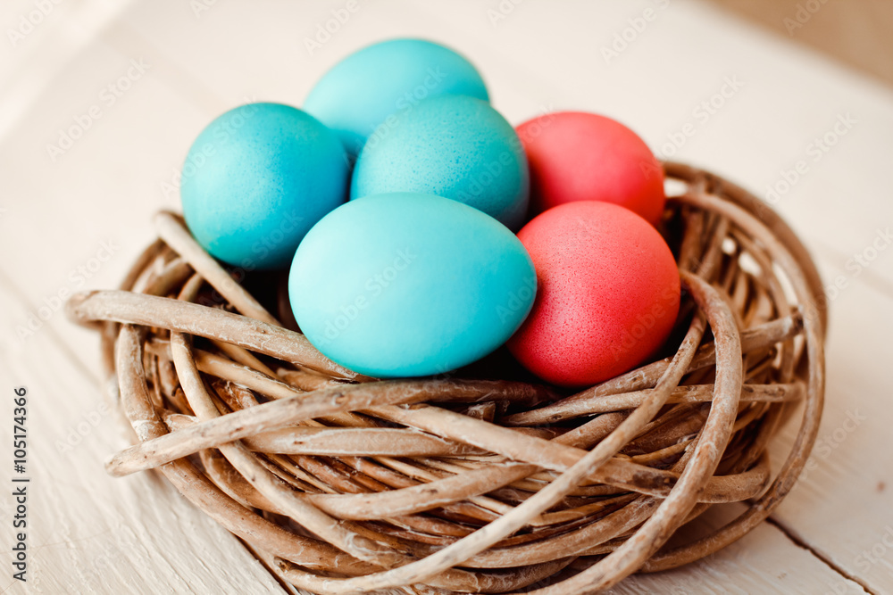 Multicolored Easter eggs in wicker basket on white wooden background Multicolored Easter eggs in wicker basket on white wooden background